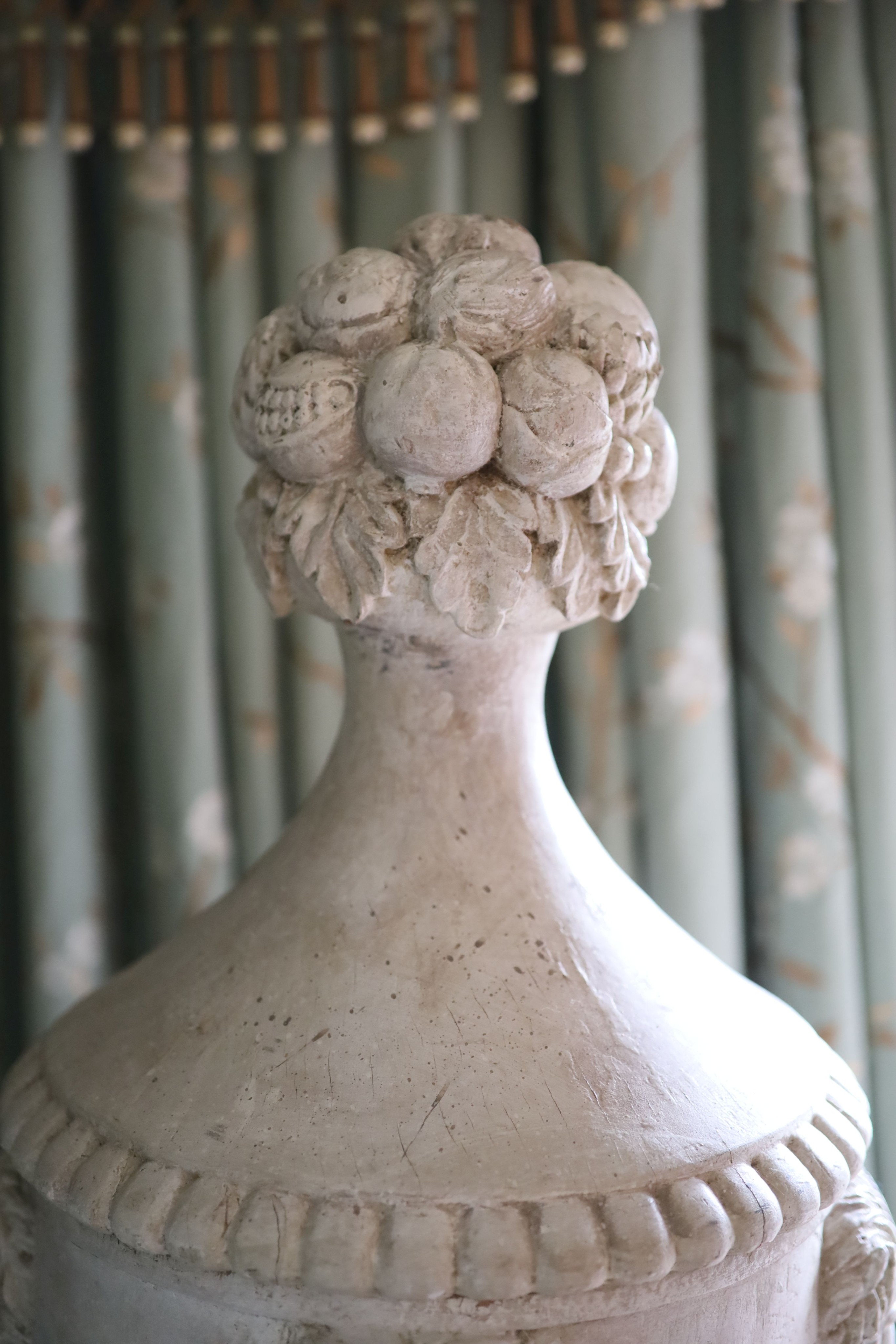 A pair of white painted carved walnut urns and covers, on wrought iron stands, the urns carved with fruit, lions masks and floral swags, height 90cm, the tapered stands with lattice work sides, height 90cm, overall heigh